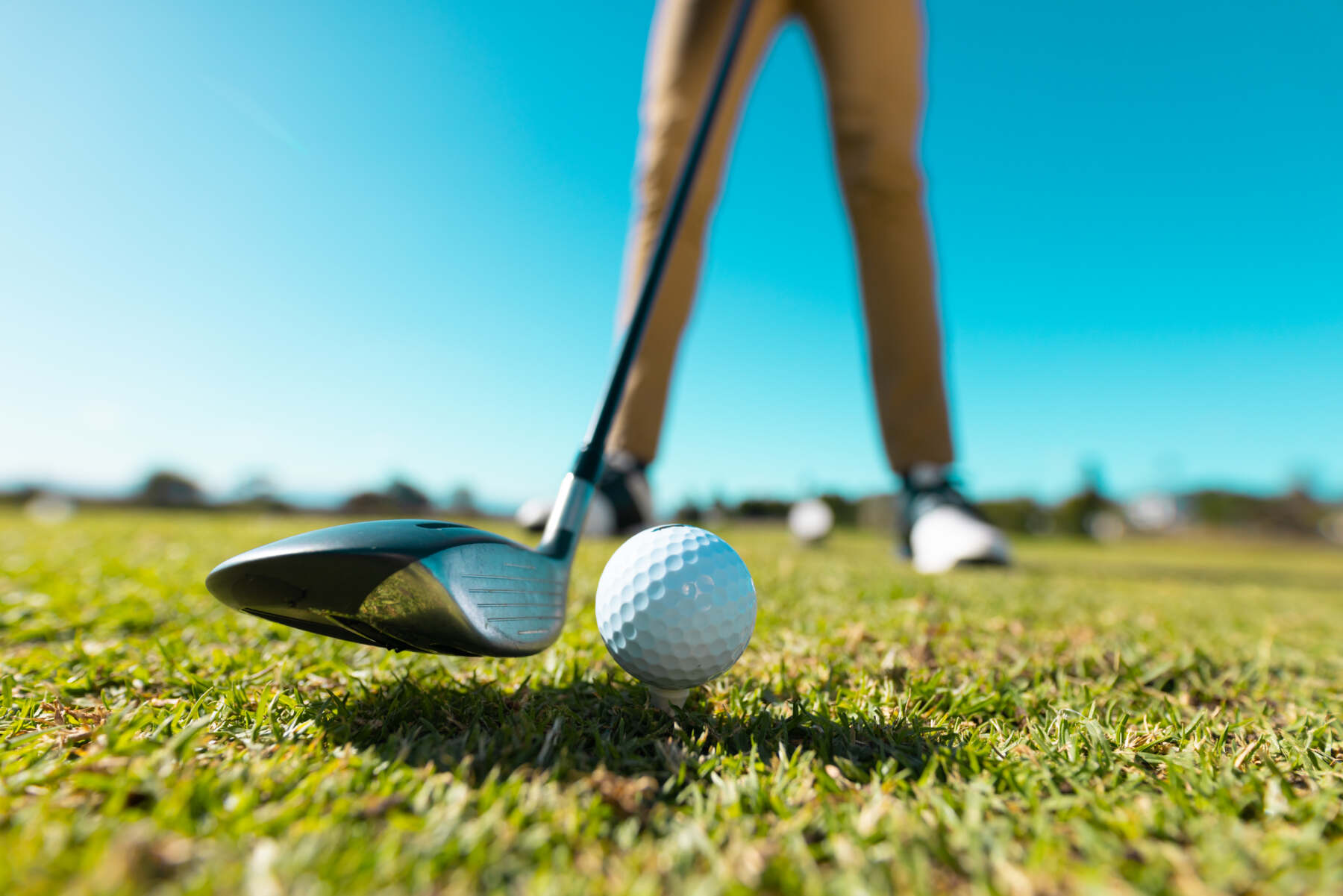 Nahaufnahme von Golfball und Driver beim Abschlag auf der Driving Range bei sonnigem Wetter. - golf trainer karlsruhe